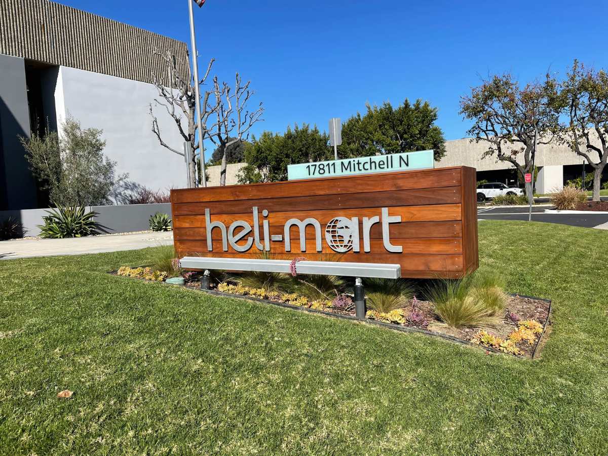 Sign for "heli-mart" at 17811 mitchell n, surrounded by greenery and blue sky. Modern design with wooden and metal elements.