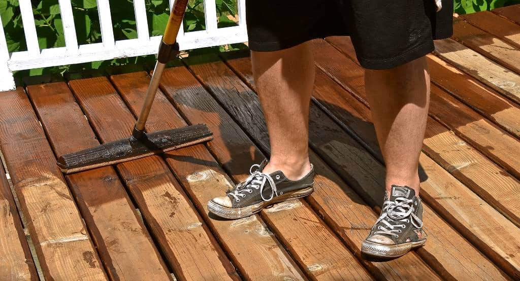 applying wood deck sealant on a sunny day
