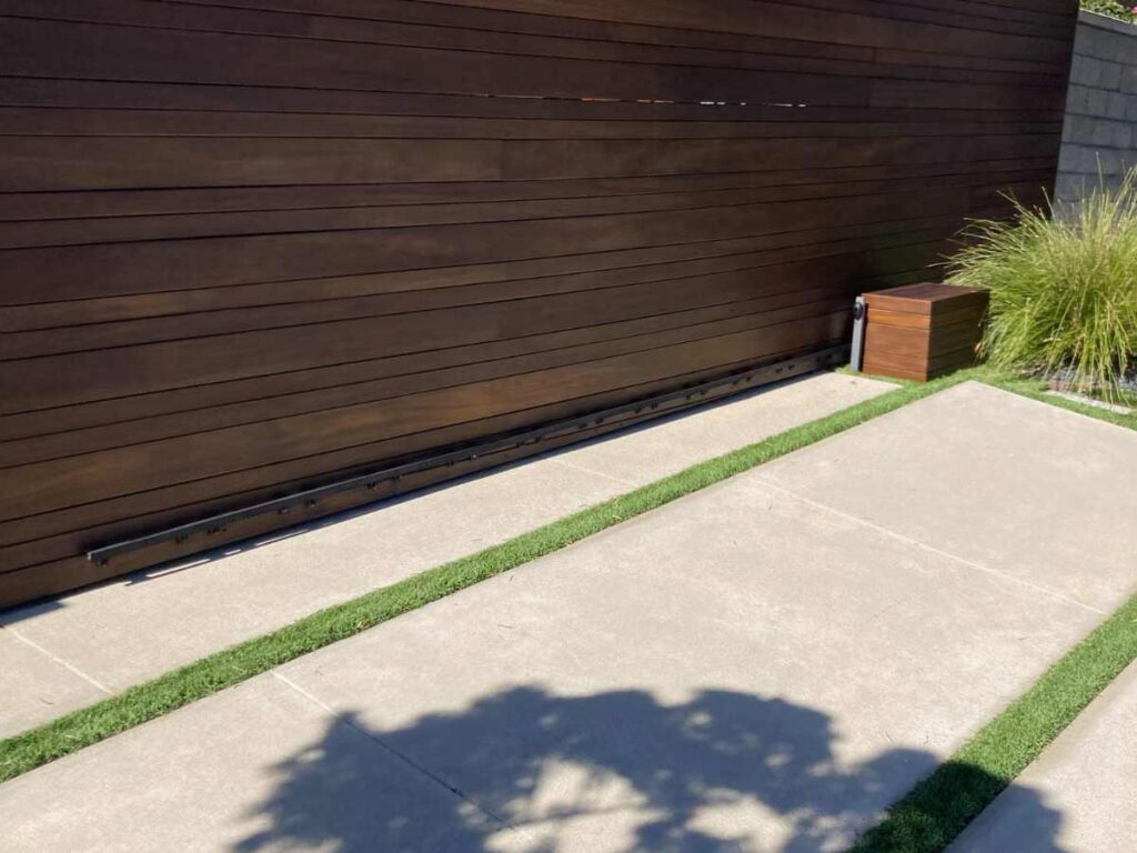 A modern wooden garage door with horizontal slats, complemented by a wooden storage box and neatly trimmed grass alongside a concrete path.