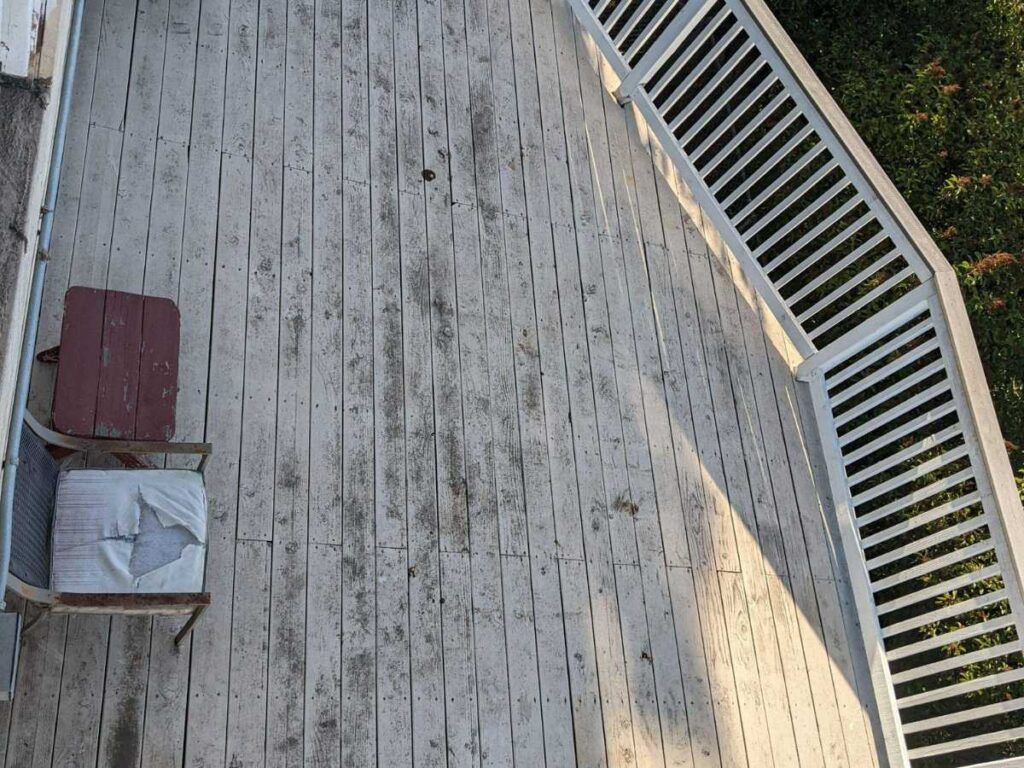 A weathered wooden deck featuring a broken chair and small red table, surrounded by a green landscape and white railing.