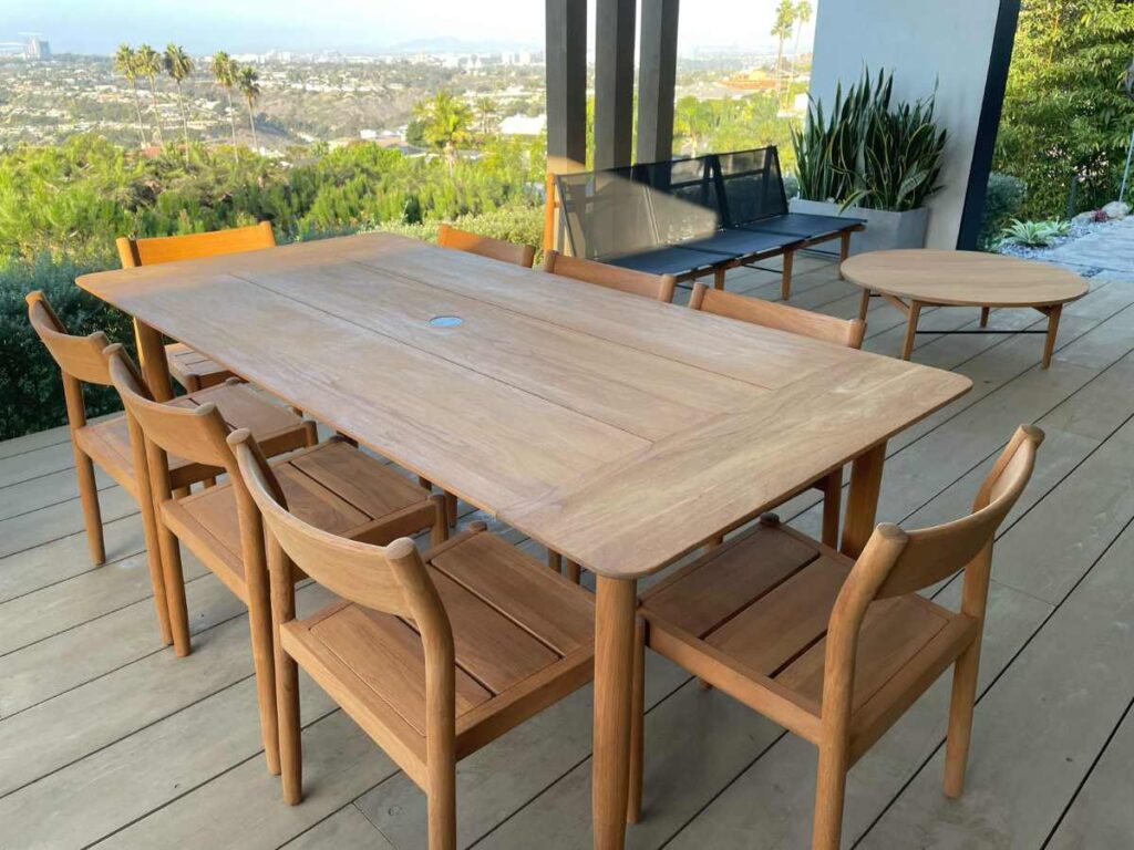 Modern wooden dining table with six chairs, surrounded by a scenic view of hills and city skyline. A cozy outdoor setting.