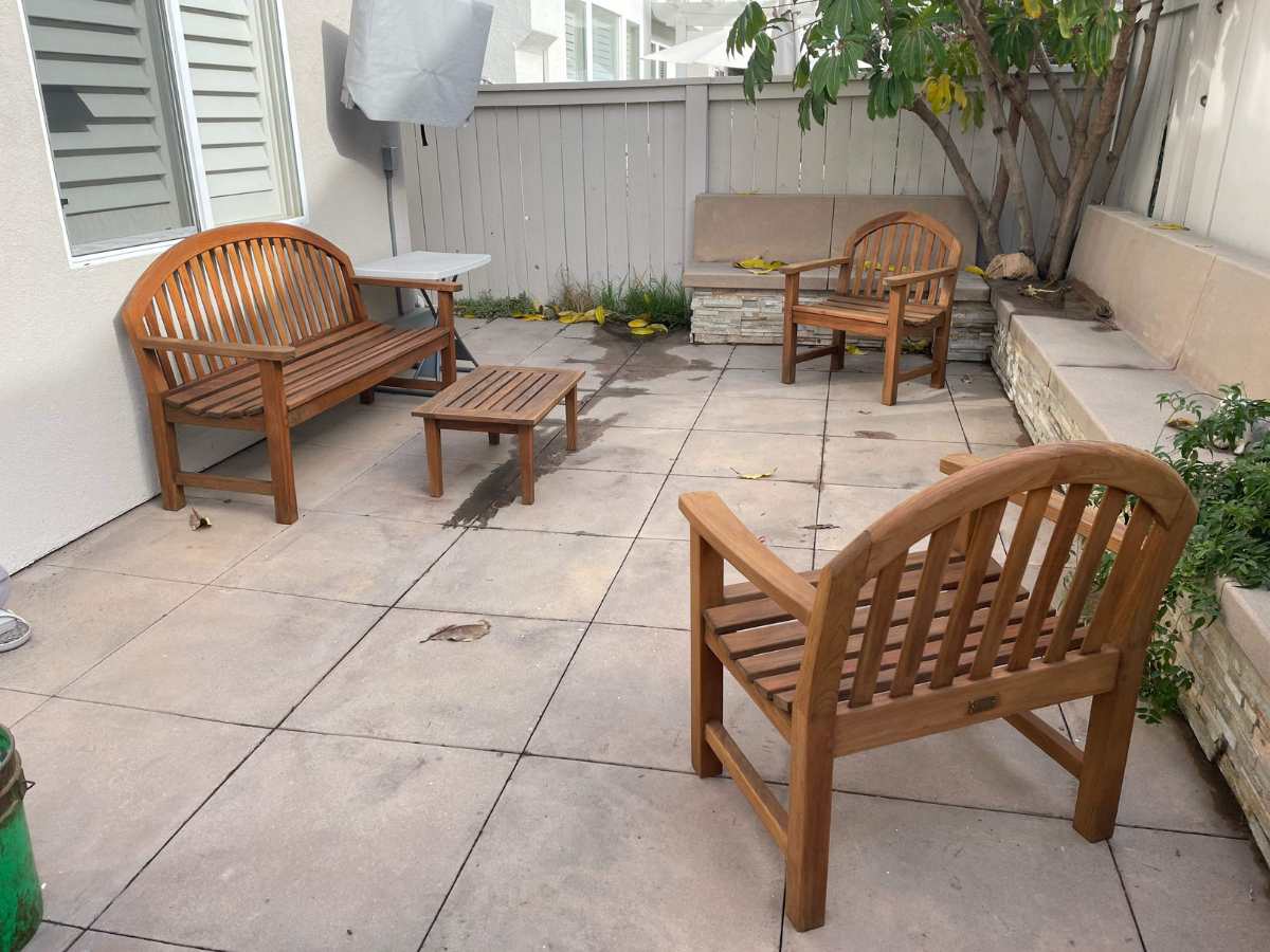 A cozy outdoor seating area features wooden benches and a small coffee table on a tiled patio, surrounded by a low fence and plants.