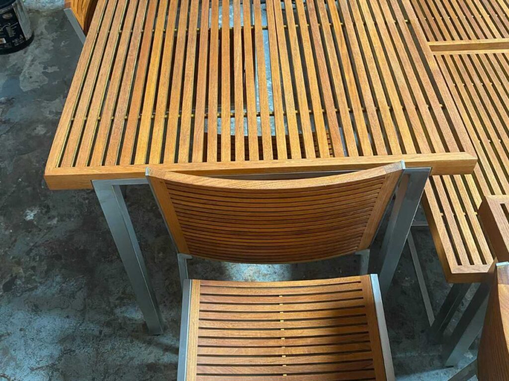 Top view of a modern wooden dining table with slatted design and matching chairs, set on a concrete floor.