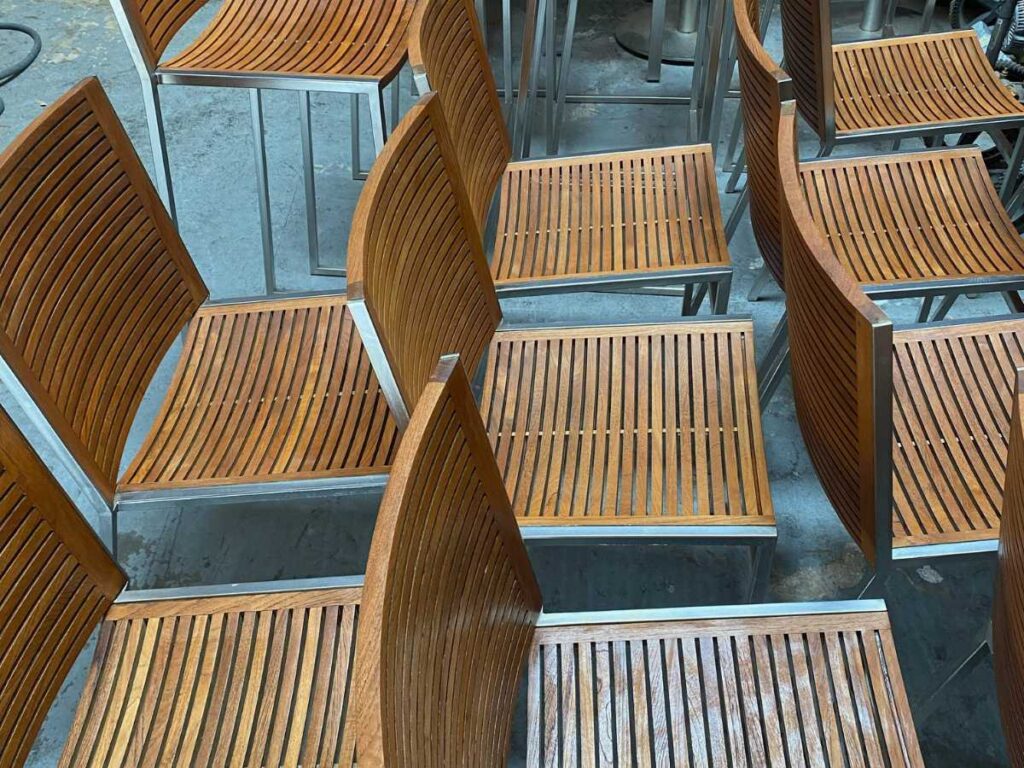 A close-up view of multiple wooden slatted chairs with metal frames arranged closely together in a workshop setting.