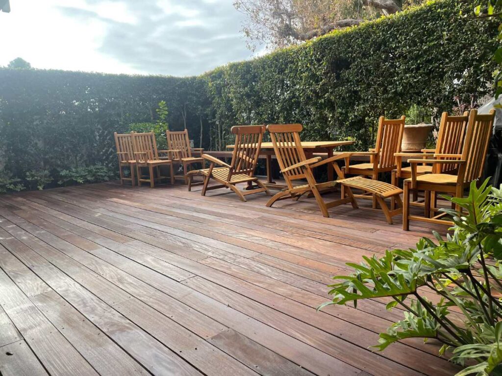 A spacious wooden deck surrounded by lush greenery, featuring multiple wooden chairs and tables for outdoor relaxation.