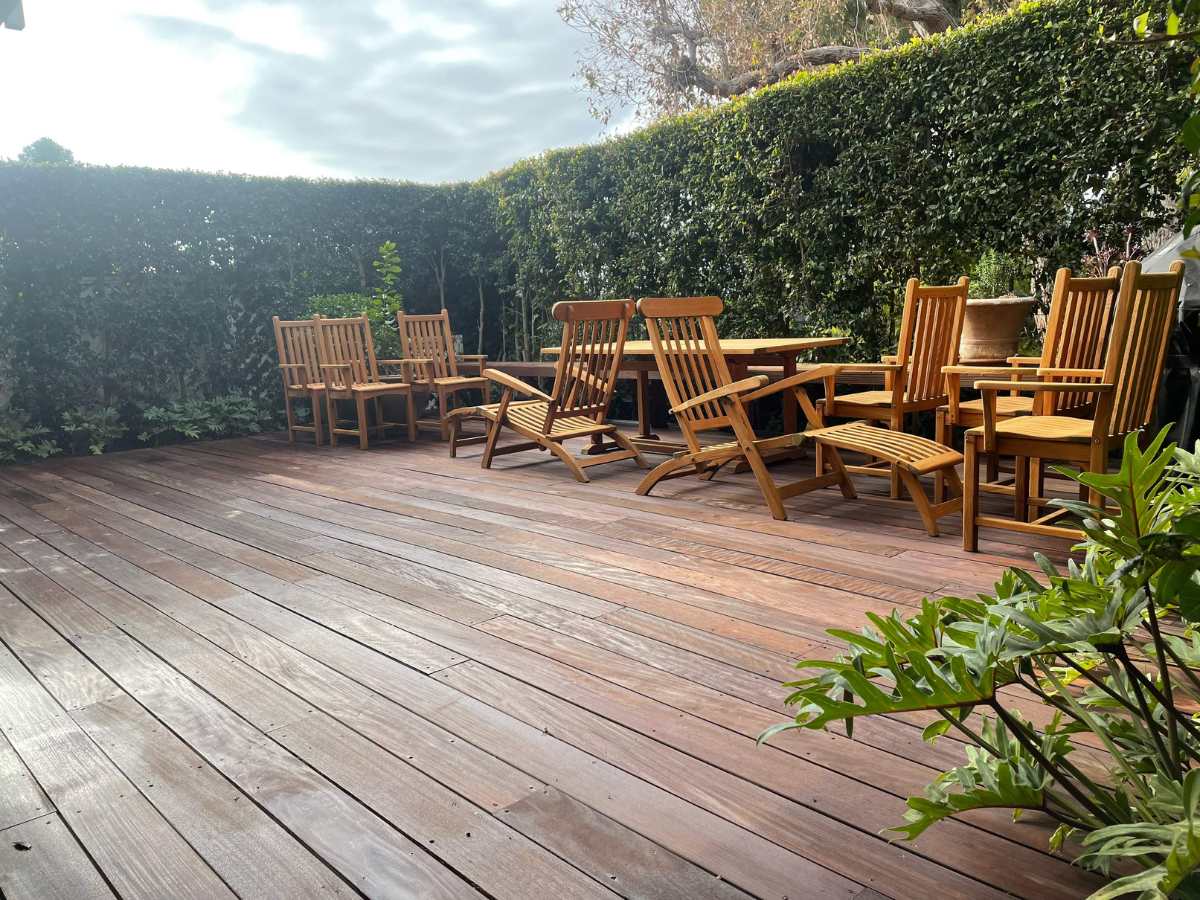 A spacious wooden deck surrounded by lush greenery, featuring multiple wooden chairs and tables for outdoor relaxation.