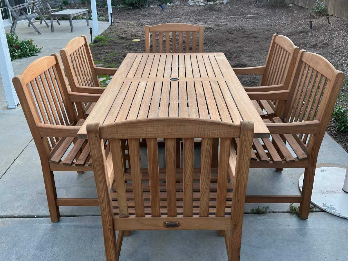 A wooden outdoor dining set featuring a slatted rectangular table and six matching chairs, set on a concrete patio.