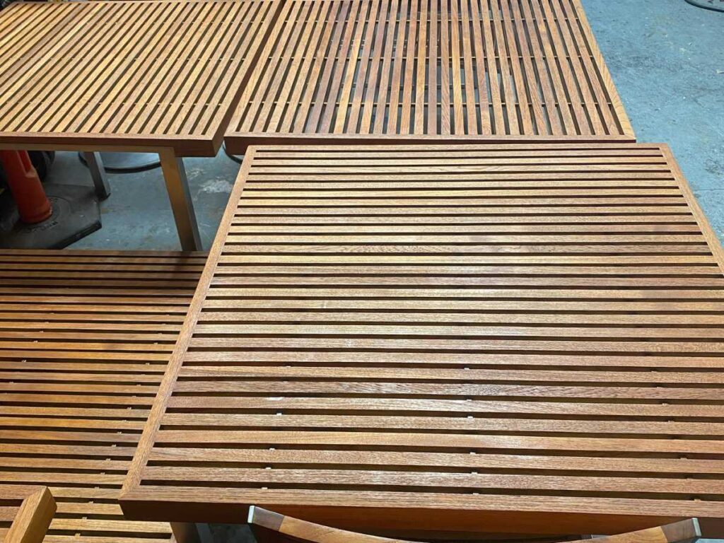 A close-up of wooden tables with slatted surfaces arranged closely together, showcasing their rich, polished grain and design.