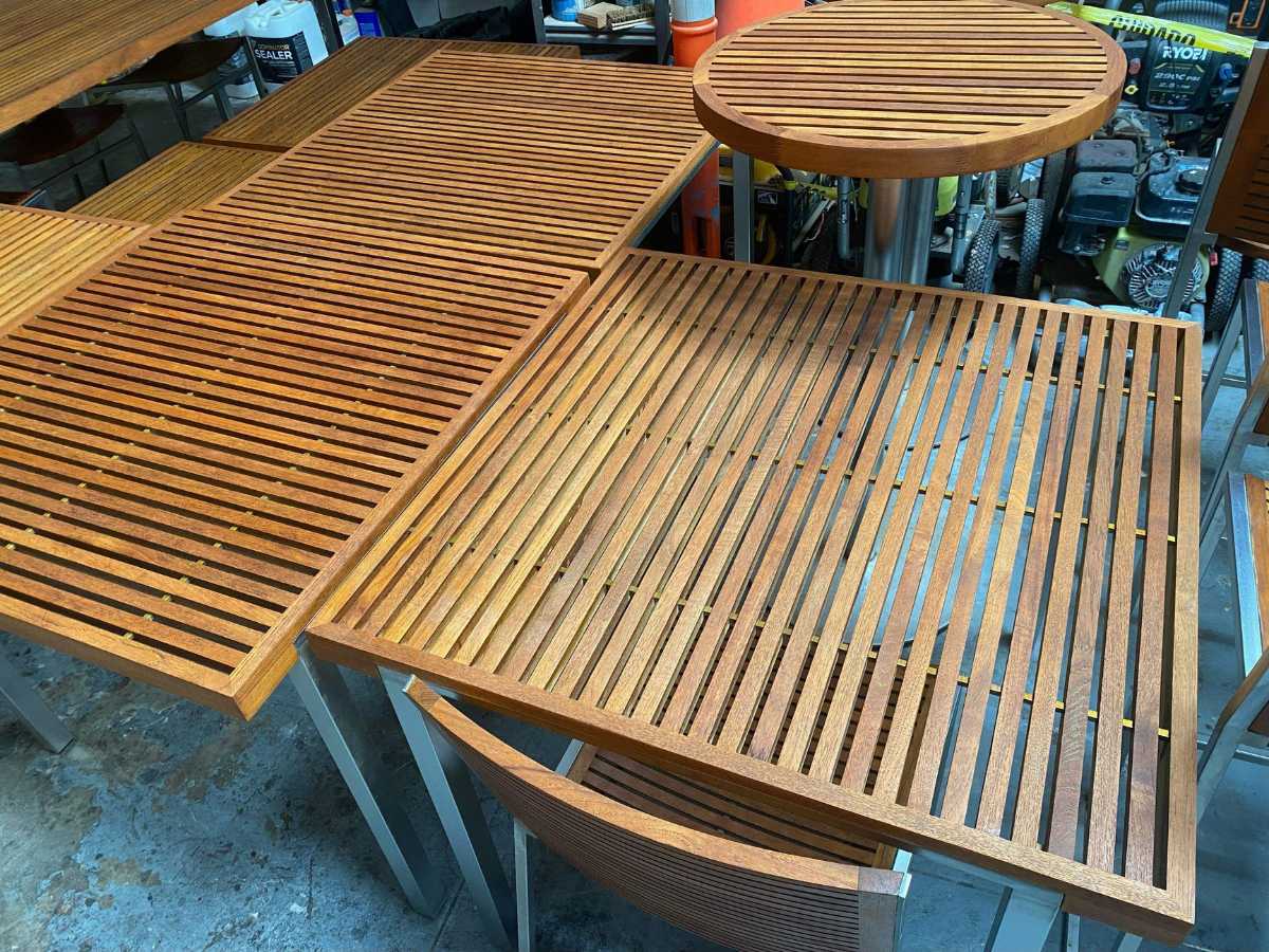 A close-up view of wooden tabletops with slatted designs, showcasing warm wood tones and metallic legs in a workshop setting.