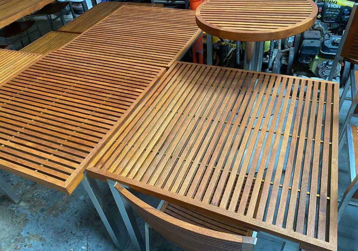 A close-up view of wooden tabletops with slatted designs, showcasing warm wood tones and metallic legs in a workshop setting.